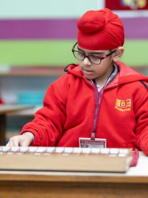 A child in a Montessori school setting focusing on an educational task, wearing a red turban and jacket.